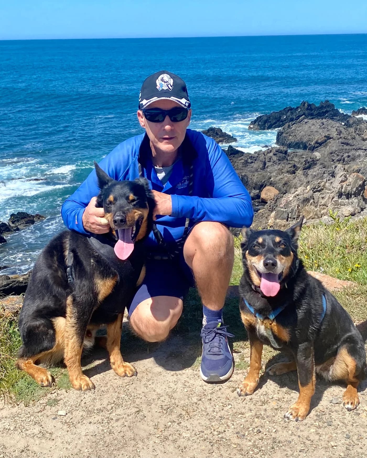 Faz crouching between his two black-and-tan kelpies on a rocky headland above the sea